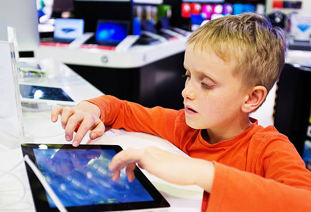 Serious schoolboy sitting in computer store trying out tablet-style pc A fascinated blond schoolboy sits in a computer store trying out the touch screen of one of a row of demonstration models of tablet-style pcs. computer shop stock pictures, royalty-free photos & images