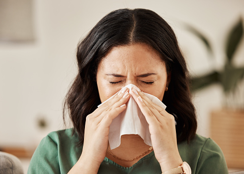 Nose, tissue and woman in a living room with flu, cold and hay fever, crisis or viral infection in her home. Sneezing, allergies and female with paper in a lounge, fever or coughing illness in house