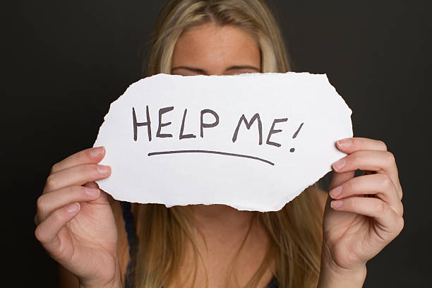 girl holding help me sign young adult hiding behing a piece of paper that says "help me" isolated on black background hostage photos stock pictures, royalty-free photos & images
