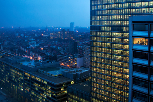 Modern glass building high above Brussels city skyline at night with illuminated offices.