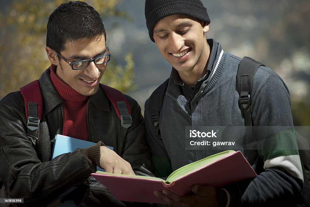 Two young adult college students discussing something in a book Close-up of two young adult college students discussing something in a book, they are standing in natural environment wearing winter dress. 20-24 Years Stock Photo