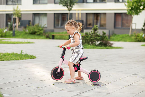 Toddler girl driving balance bike outdoors. Learning to ride bike concept. Urban.