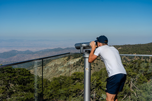 Side-view image of young male hiker looking through tourist binoculars
