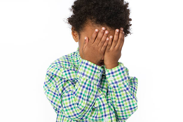 little boy hiding behind his hands as a shyness or sadness concept isolated on white background