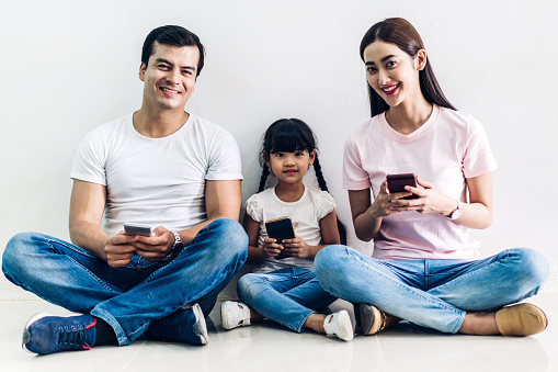 Happy family father and mother with daughter sitting and use technology together of smartphone on wall background