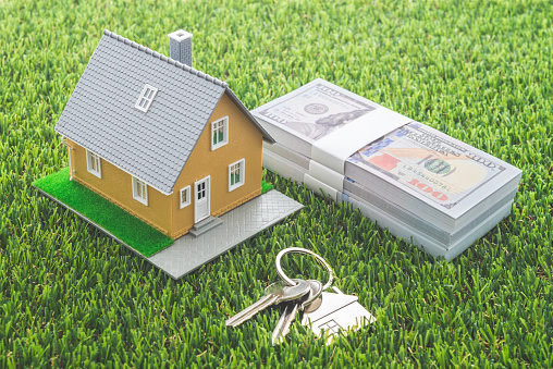 House model, bill dollar banknotes and key on green artificial grass background. Money saving for new house, home mortgage loan and real estate property business concept.