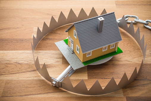 Mortgage house in a trap on wooden table background. House trapped on debt or loan problem or risk in real estate property financing, real estate agency fraud concept.
