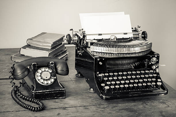 máquina de escribir vintage, teléfono, viejos libros en la tabla desaturado photo - typewriter typing machine old fotografías e imágenes de stock