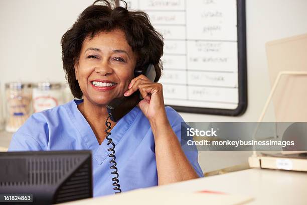Nurse Making Phone Call At Nurses Station Stock Photo - Download Image Now - Nurse, Using Phone, Receptionist