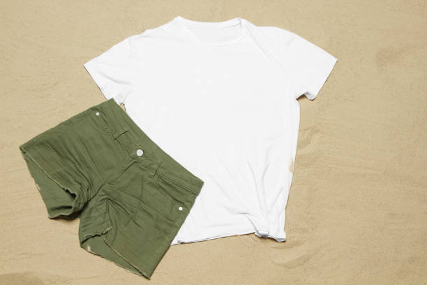 istock Mockup white not wrinkled summer t-shirt copy space. Sand beach texture background. Blank template woman man shirt Top view. Summertime accessories. Flat-lay closeup tshirt on seashore. Beachtime 1618248654
