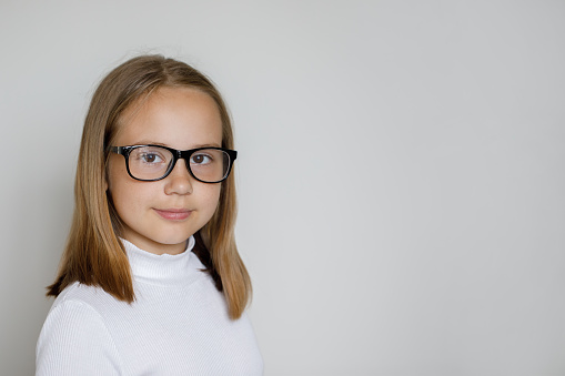 Portrait of smart young girl in glasses on white studio wall background