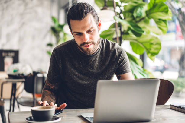 istock Handsome bearded hipster man use and looking at laptop computer with coffee at table in cafe.Communication and technology concept 1618277479