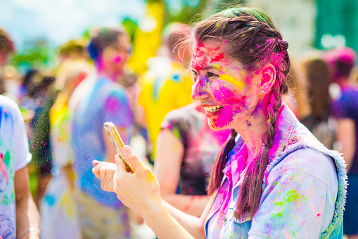 Khakiv, Ukraine - 19 May 2018: Cheerful girl having fun at the holi color festival. Portrait of pretty smiling girl with multicolored face at the holiday of colors