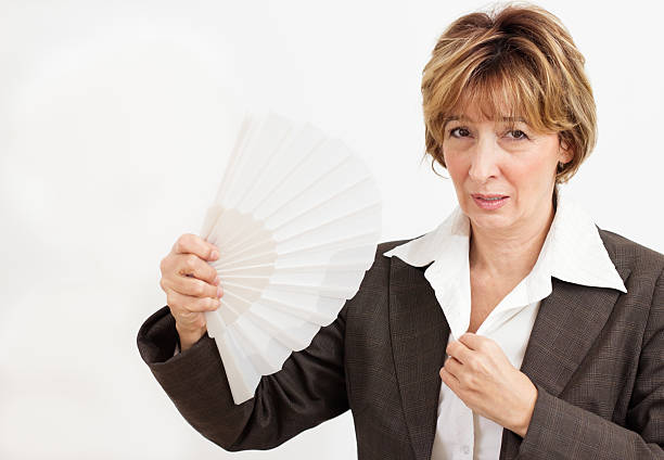 Businesswoman in suit fanning herself with a paper fan stock photo