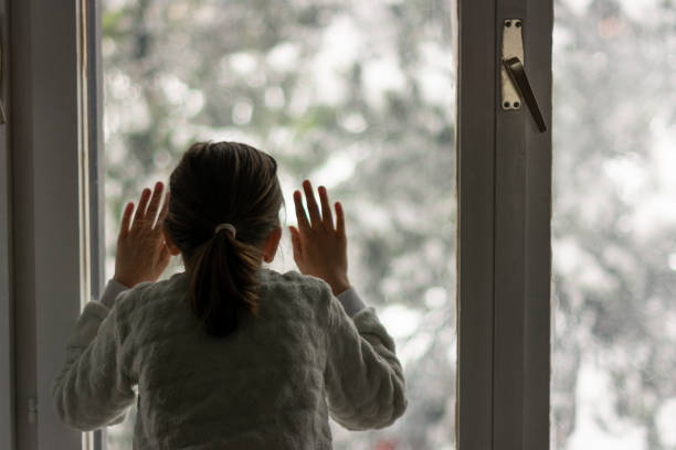 istock Girl looking through the window at snowy day 1618299972