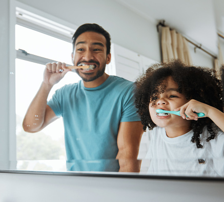 Father, son and brushing teeth together in mirror, bathroom or home for hygiene, teaching or oral care. Man, child and toothbrush with foam, cleaning and learning for health, mouth and dental results