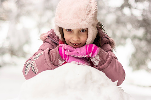 Cute little girl playing whit snow during winter day in the yard