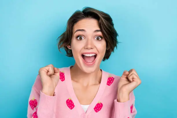 Photo of Portrait of glad cheerful girl wear stylish clothes raise hands fist rejoice win lottery shout yeah isolated on blue color background