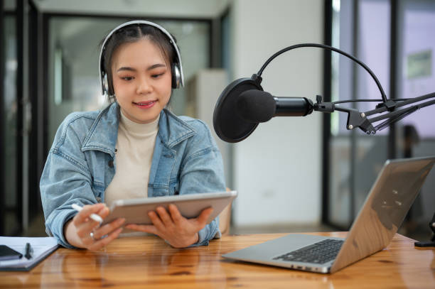 istock A beautiful Asian female radio host is looking at her tablet screen, speaking into a microphone 1618312810