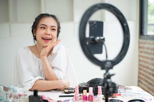 An attractive and happy young Asian female beauty blogger recording her makeup tutorial video in her home studio. content creator, influencer, fashion and beauty blogger