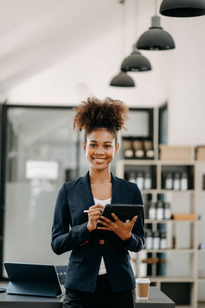 istock Confident beautiful African businesswoman typing laptop computer and digital tablet while holding coffee at office 1618325264