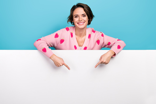Photo of nice girl wearing pink trendy jumper directing fingers empty space paper wall proposition sale isolated on blue color background.
