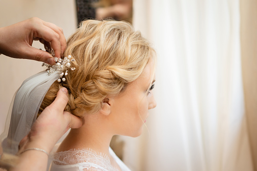 Hairdresser stylist pins a veil in the bride's hair for a wedding ceremony