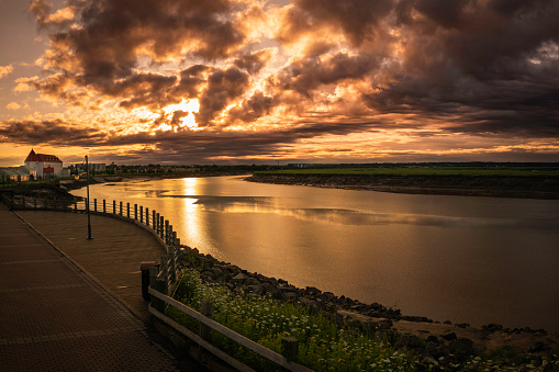Petitcodiac River with dramatic sunrise cloudscape at Bore Park or Parc Bore Riverfront Walk, a popular place to watch the tidal bore in Moncton, New Brunswick, Canada