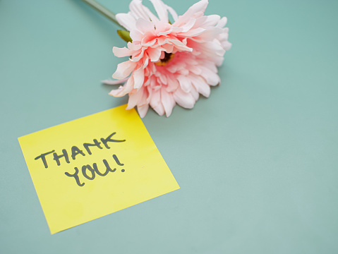 Top view of words thank you written on sticky note with flowers beside