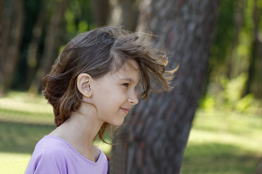 Cute young girl with windy brown hair walking in park, face closeup