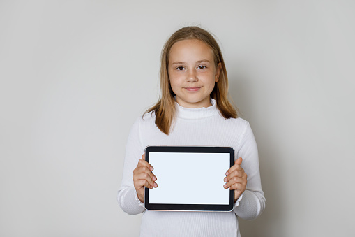 Smiling young child girl holding tablet gadget with empty white screen display for new application or mobile website, Mockup banner