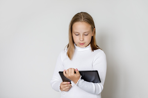 Pretty serious child using tablet gadget on white studio wall background