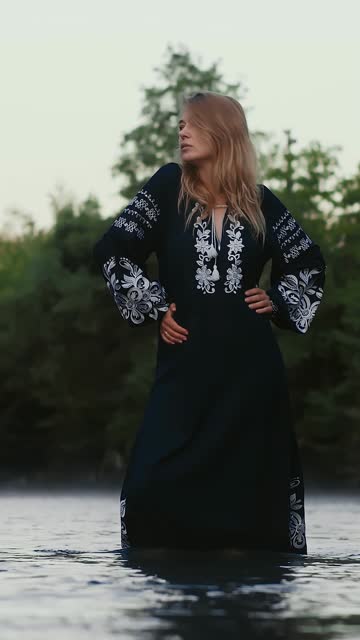Vertical video romantic blonde girl, woman in a long national dress posing in a mountain river shrouded in morning mist