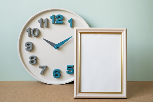 Blank picture frame with clock on brown shelf. mint wall background. copy space