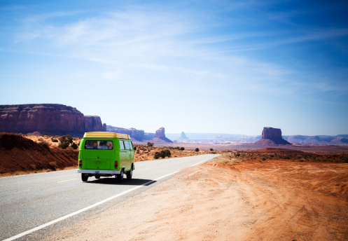 Green van driving on the Highway 163 in the Monument Valley between Utah and Arizona during a bright blue day. Car in motion.