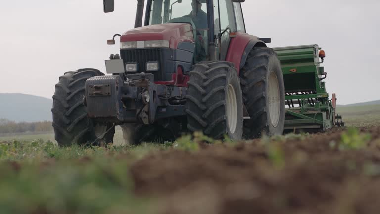 Spring sowing season. Farmer with a tractor sows corn seeds on his field. Planting corn with trailed planter. Farming seeding. The concept of agriculture and agricultural machinery, slow motion