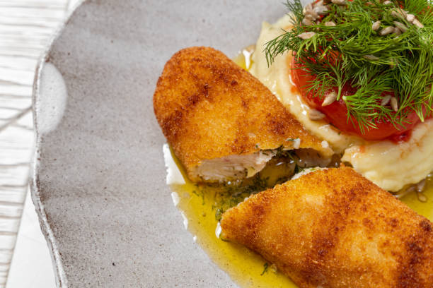 istock Chicken Kiev cutlet breaded with butter and herbs inside, mashed potatoes, tomato and microgreens on top. Food lies in a light ceramic plate on a light background. 1618437326