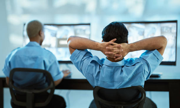Security guard, safety and team in control room with a computer screen for surveillance. Behind a man and woman officer relax in office for crime investigation with cctv monitor and camera footage