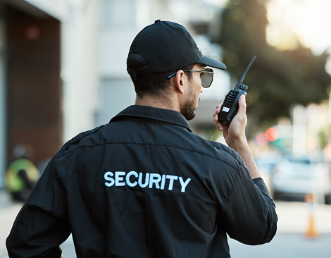Radio, man and a security guard or safety officer outdoor on a city road for communication. Back of a person with a walkie talkie on urban street to report crime for investigation and surveillance