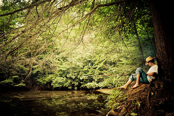 young boy fishing in a pond while leaning on a  big tree - with a retro vintage look