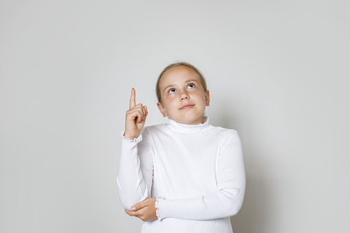 Cute child girl 10 years old pointing up against white studio wall background