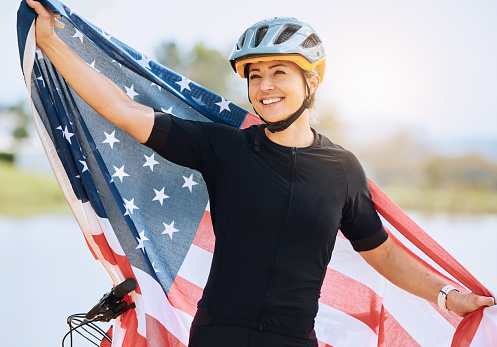 Fitness, American flag and woman with smile, biker and victory with competition, workout and training. Female athlete, happy person and cyclist with symbol for USA, winning and happiness with success