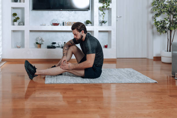 istock Injured young man seated on exercise mat, holding his leg 1618476419