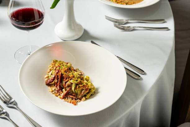 istock Spinach pasta with dried tomatoes and nuts with chopped green onions in a light ceramic plate. The dish stands on a light tablecloth, next to a glass of red wine and cutlery. 1618487280