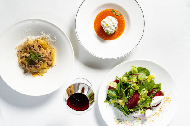 Spinach pasta with sun-dried tomatoes, eggplant breaded with stracciatella cheese and salad with beetroot and gorgonzola in a light ceramic plate on a light tablecloth. Nearby is a glass of red wine.