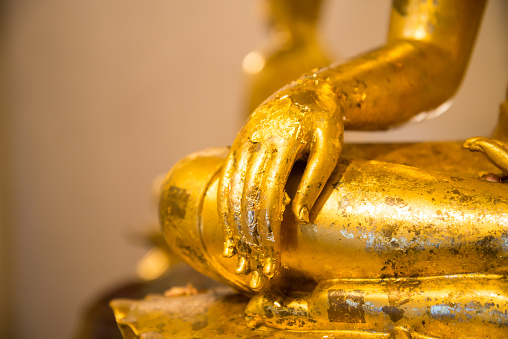 Close up hand of a golden sitting buddha statue in temple. Buddhism religion, meditation concept.