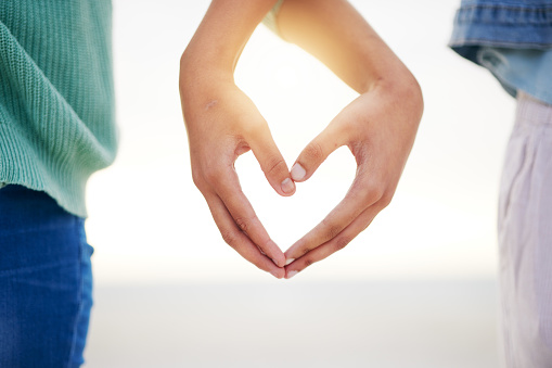 Closeup, beach and couple with heart hands, marriage and relationship with growth, loving and bonding. Zoom, people and lovers with symbol for love, support and social media with gesture and romance