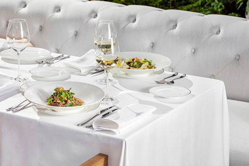 Steak with chanterelle mushrooms and salad with trout in light ceramic plates on a light tablecloth. There are glasses of red and white wine nearby.