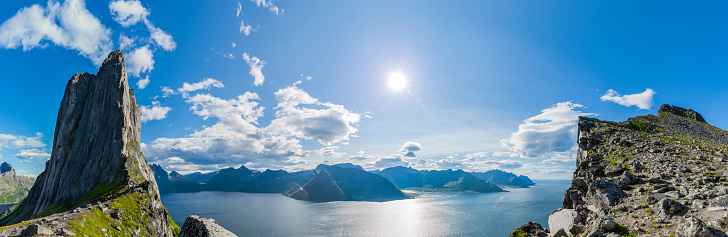 Drone high-angle photo of the motor vehicles passing the beautiful road with view of the mountain peaks and the ocean during bright summer sunset in Northern Norway