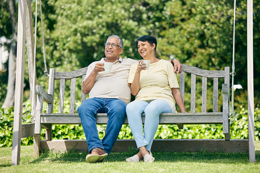 Shot of a senior Caucasian couple enjoying coffee while sitting on a bench in a public park. Smiling enjoying life.